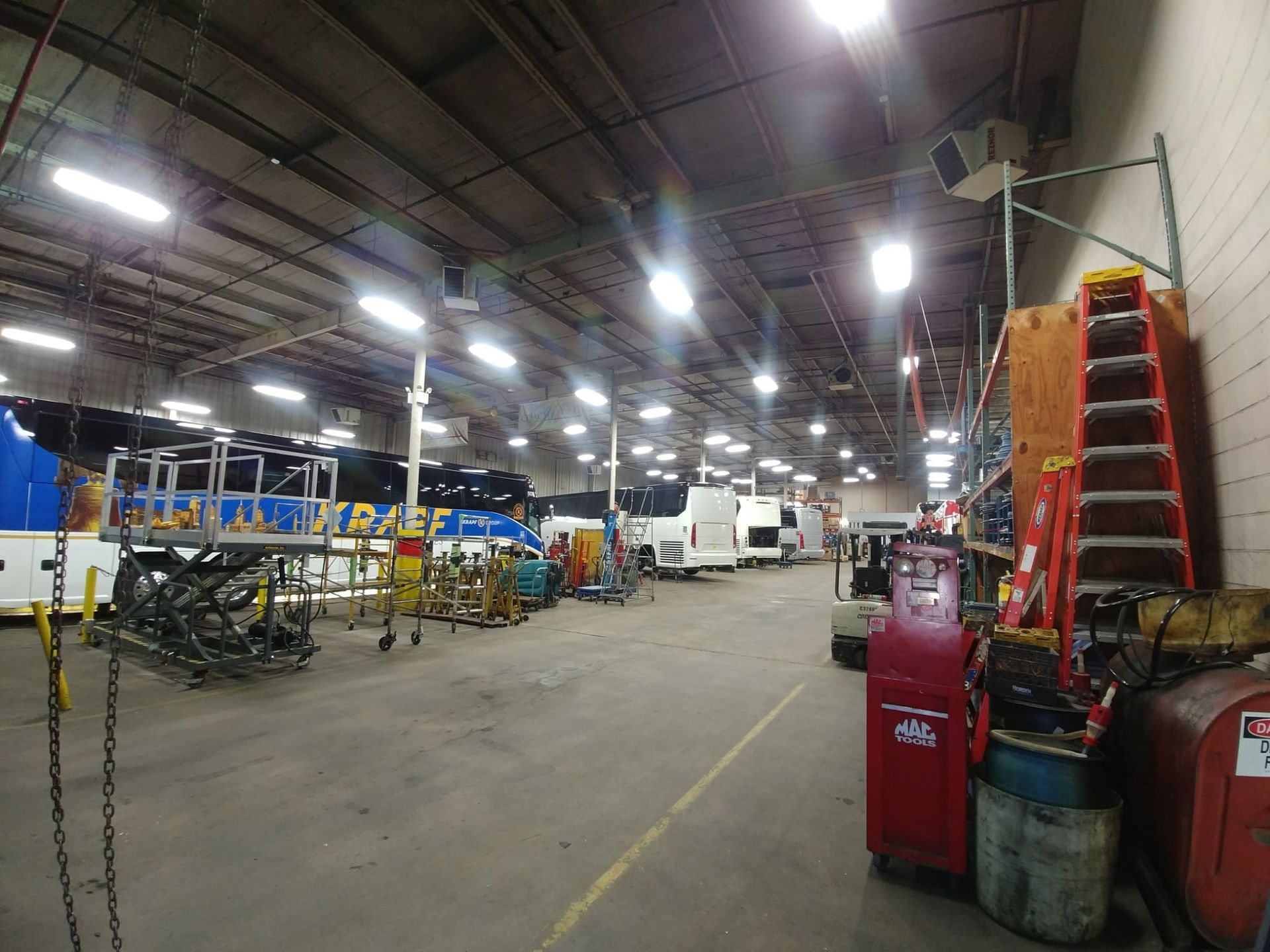 Large warehouse with machinery, overhead lights, and stacked equipment, viewed from the center aisle