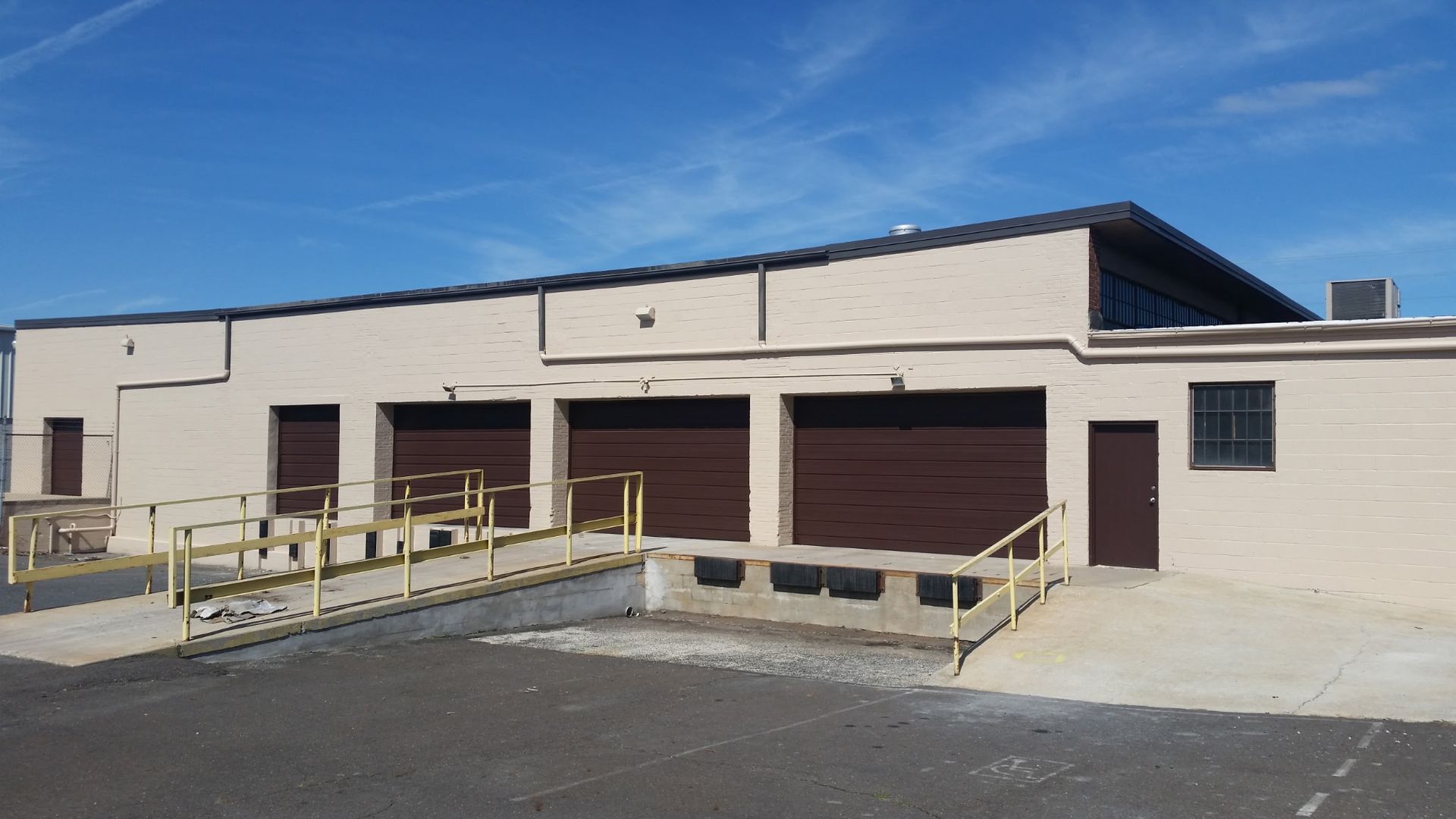 Beige industrial warehouse with roll-up doors and a wheelchair-accessible loading ramp