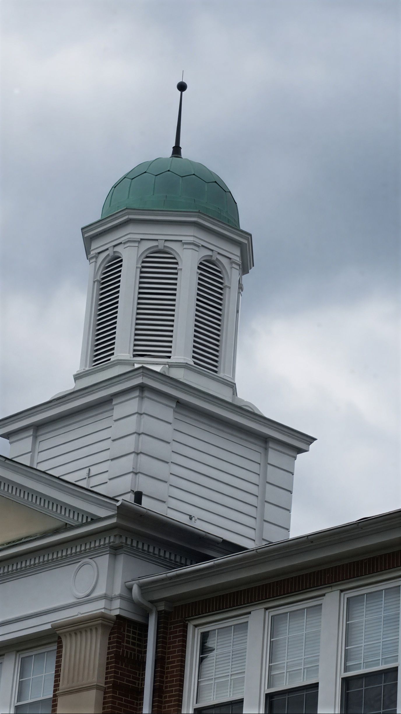 White building tower with green dome and cupola against a cloudy sky