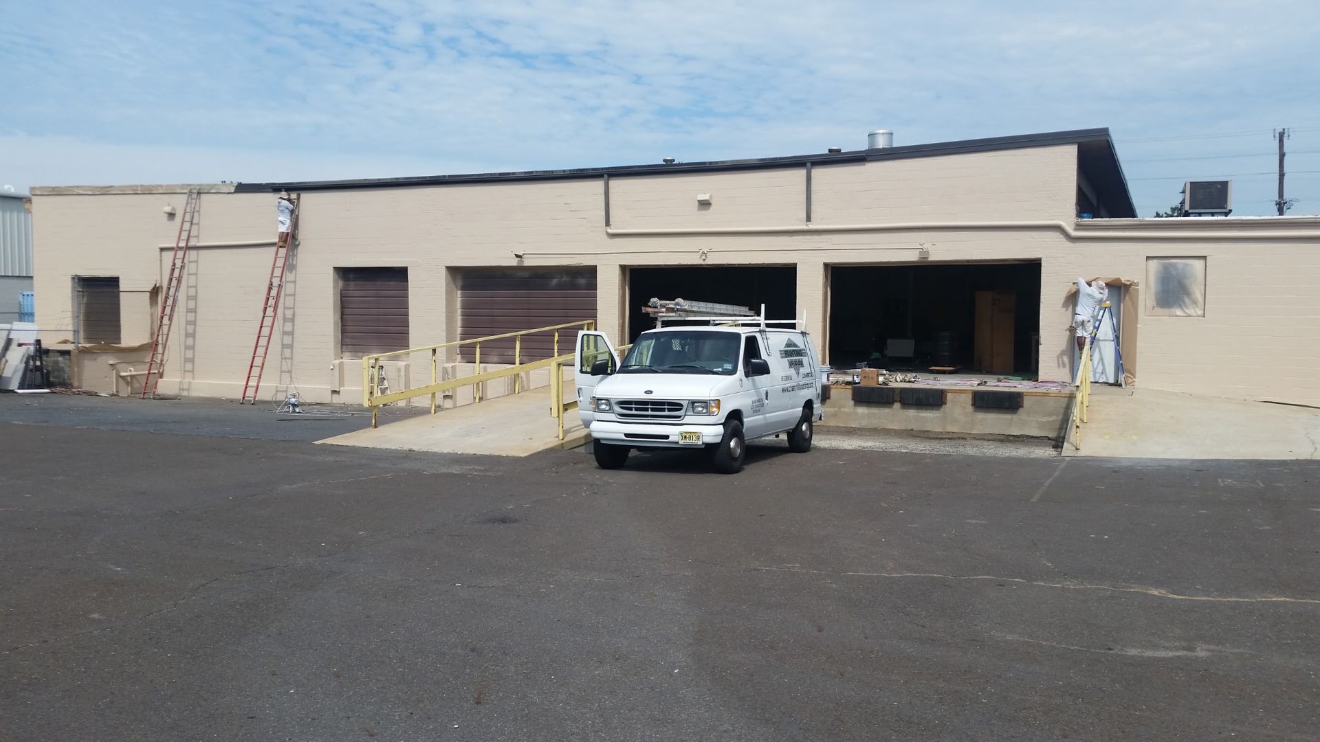 A beige industrial building with a white truck parked in front and a ladder leaning against the left side.