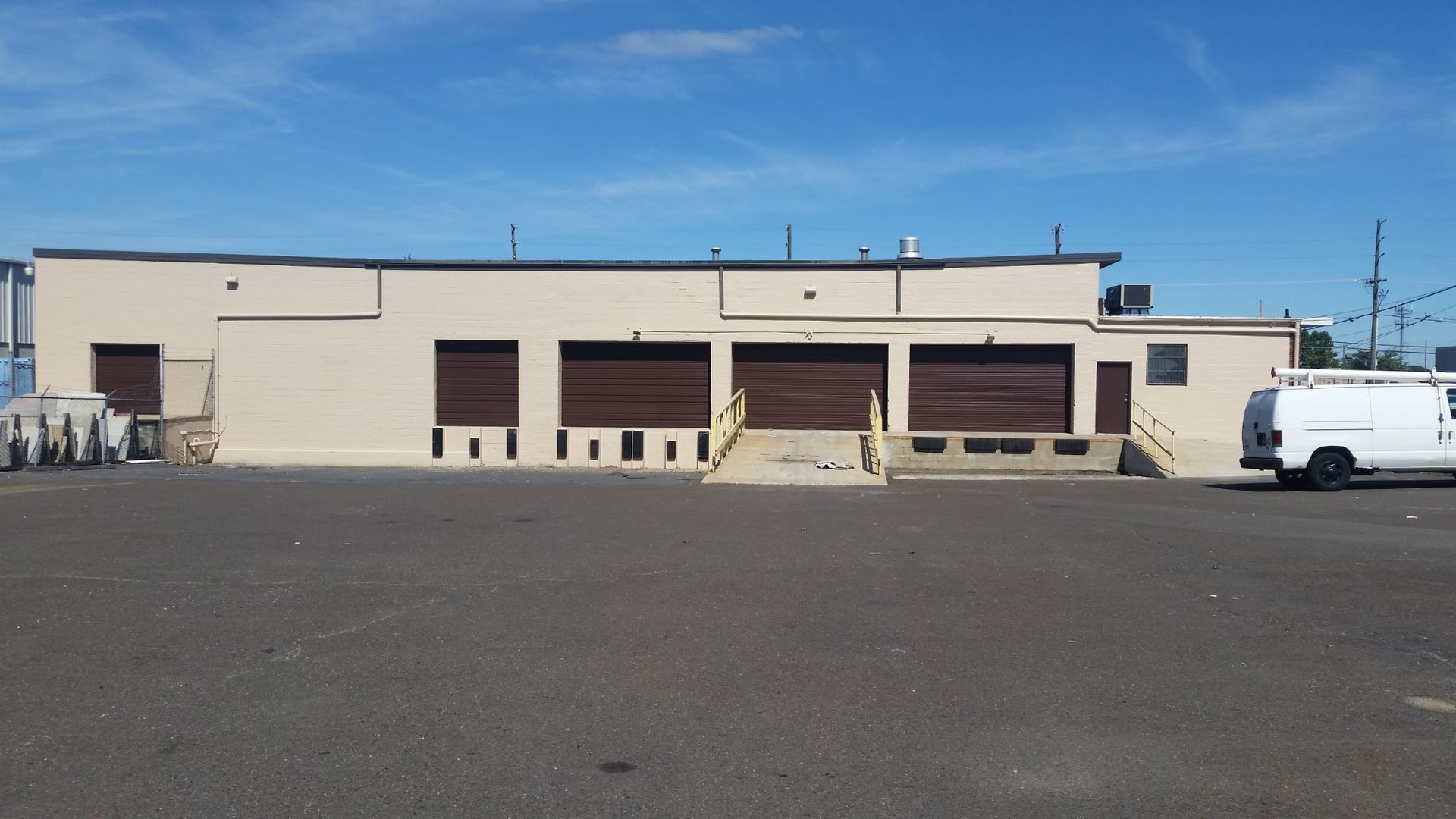 Low beige industrial building with loading docks and a white van in a parking lot under a clear sky