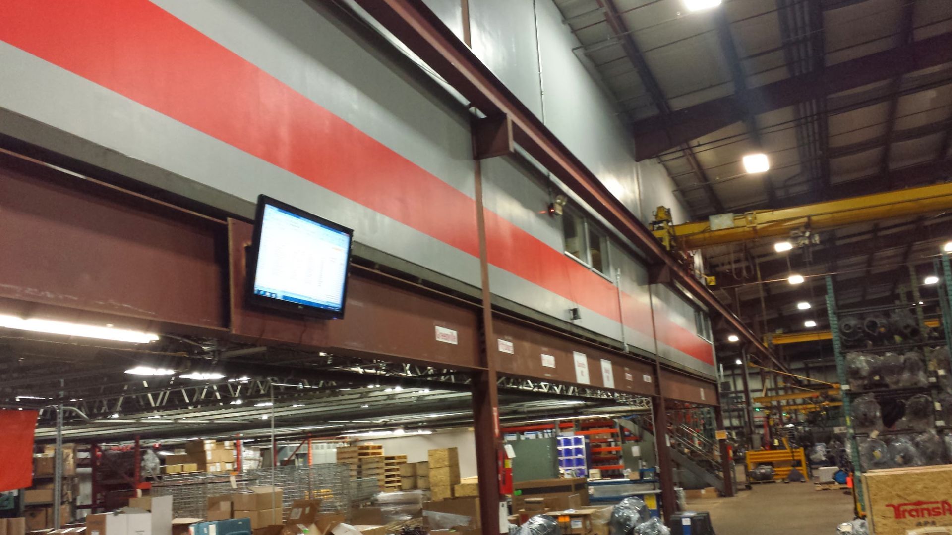 Interior of a large industrial warehouse with a red stripe and a wall-mounted monitor above work areas