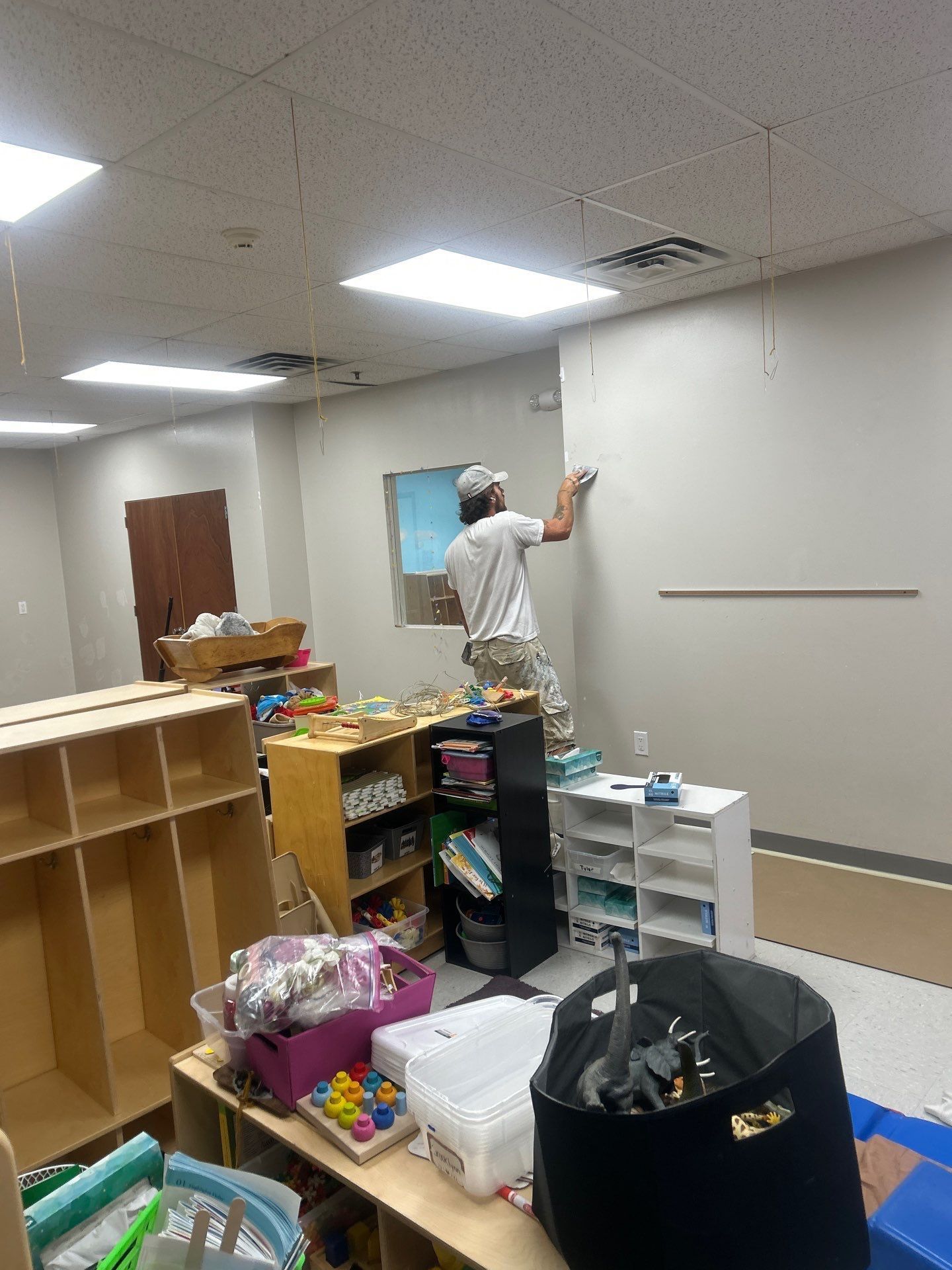 Person painting a ceiling panel in a cluttered room with shelves, boxes, and tools.