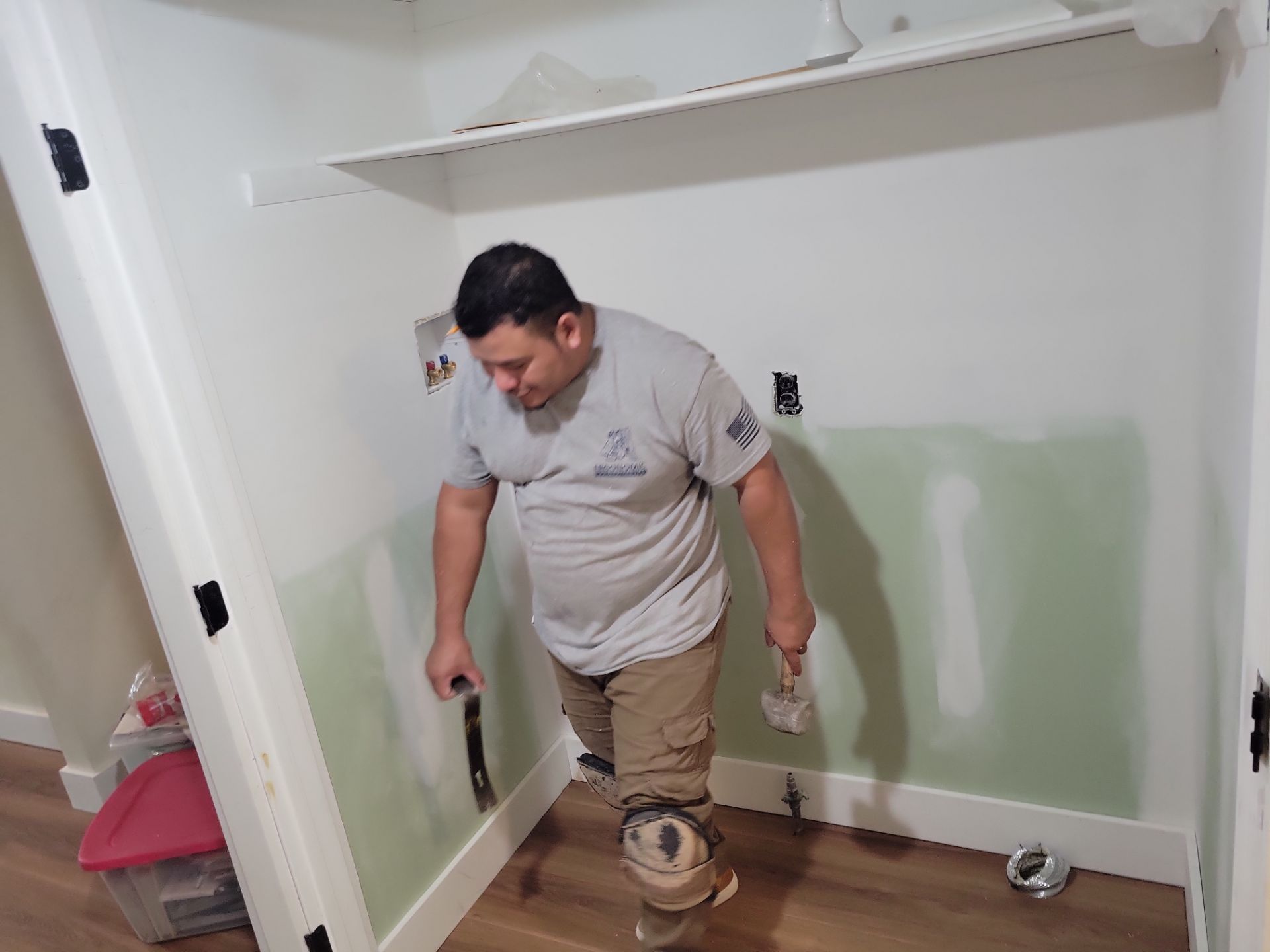 Person standing in a small room under renovation, holding tools near unfinished walls and floor