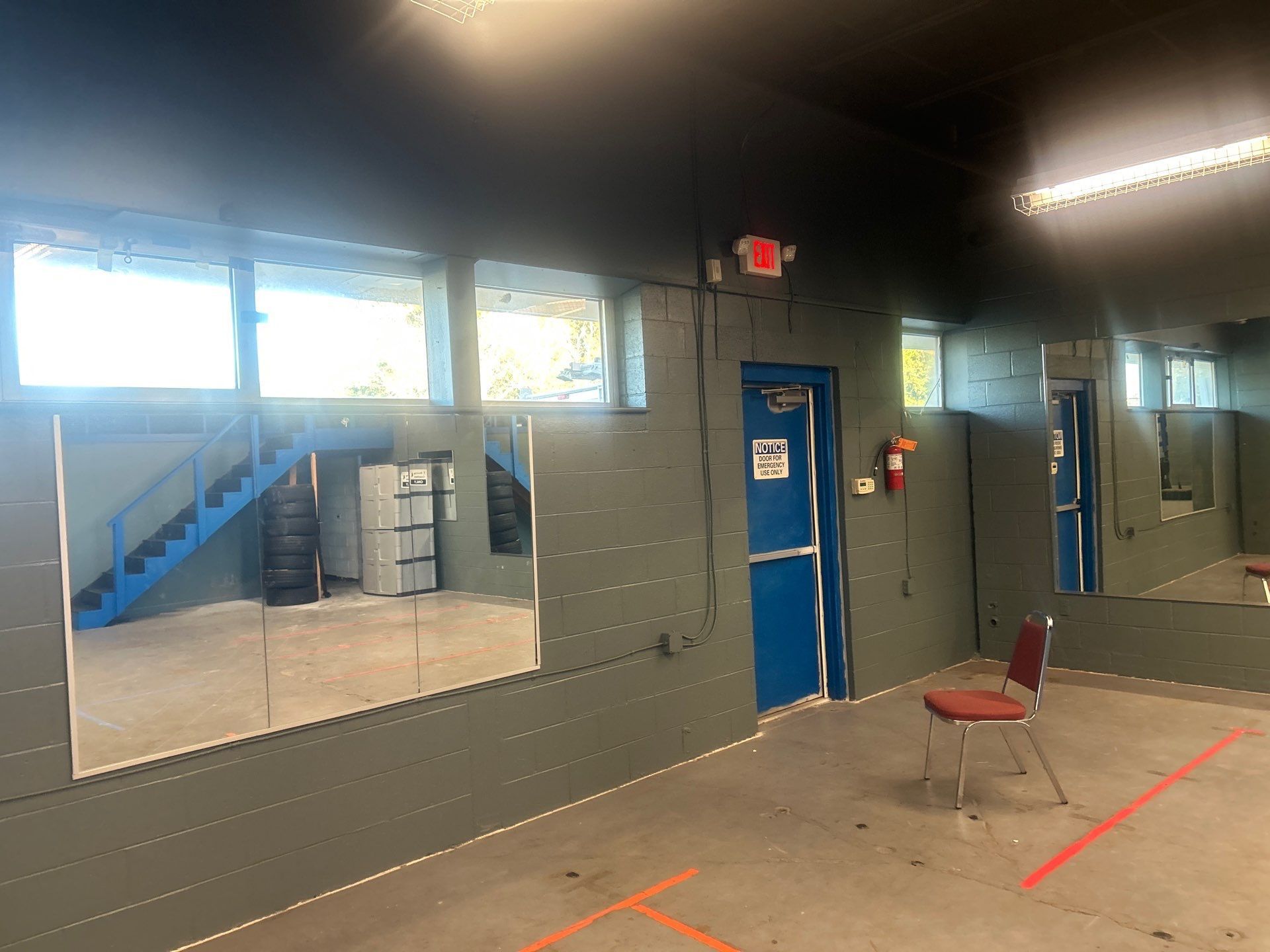 Empty room with gray walls, blue door, mirrors, and a red chair on a taped floor.