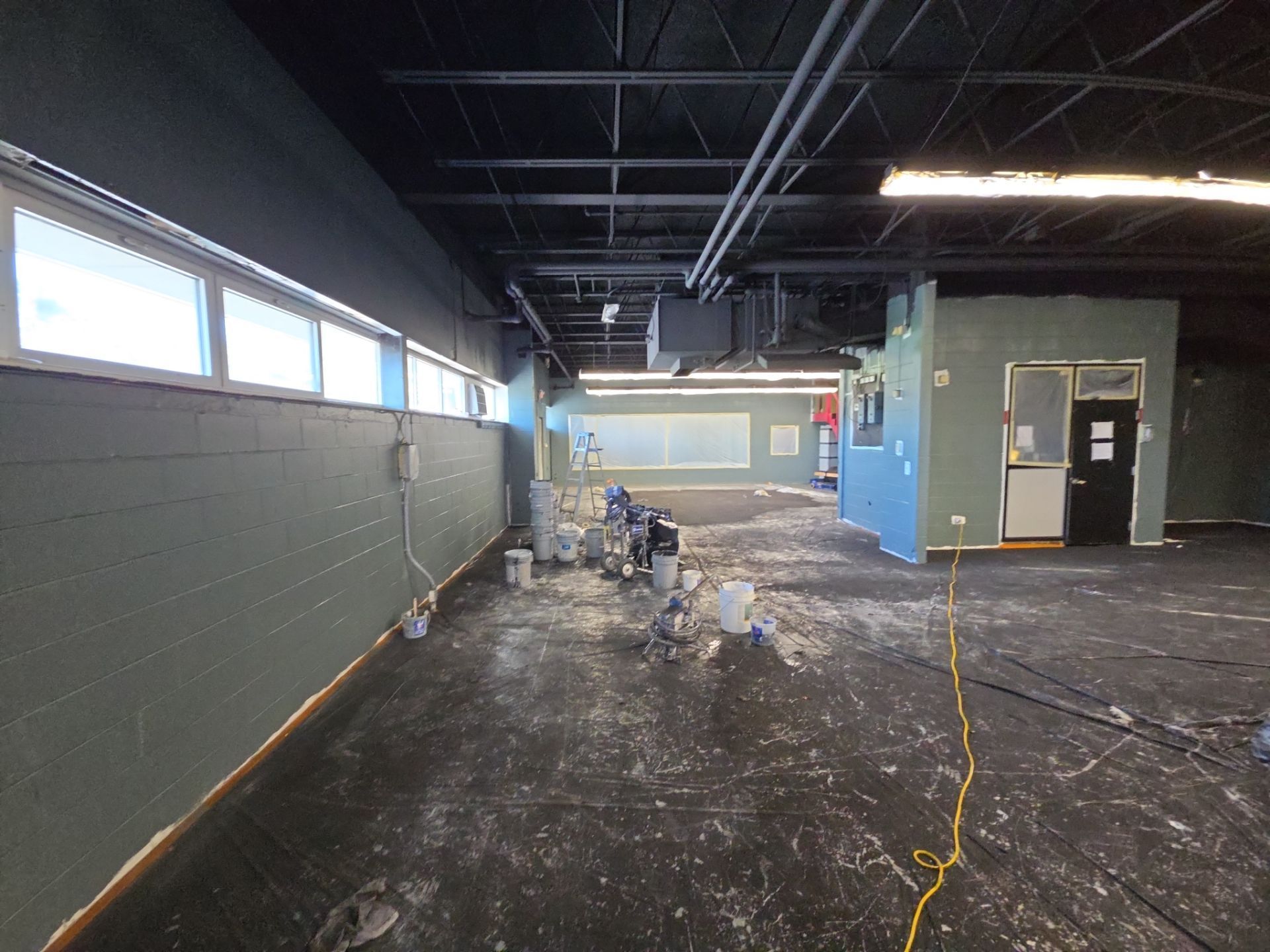Empty room under renovation with blue walls, dark floor, and exposed ceiling pipes.