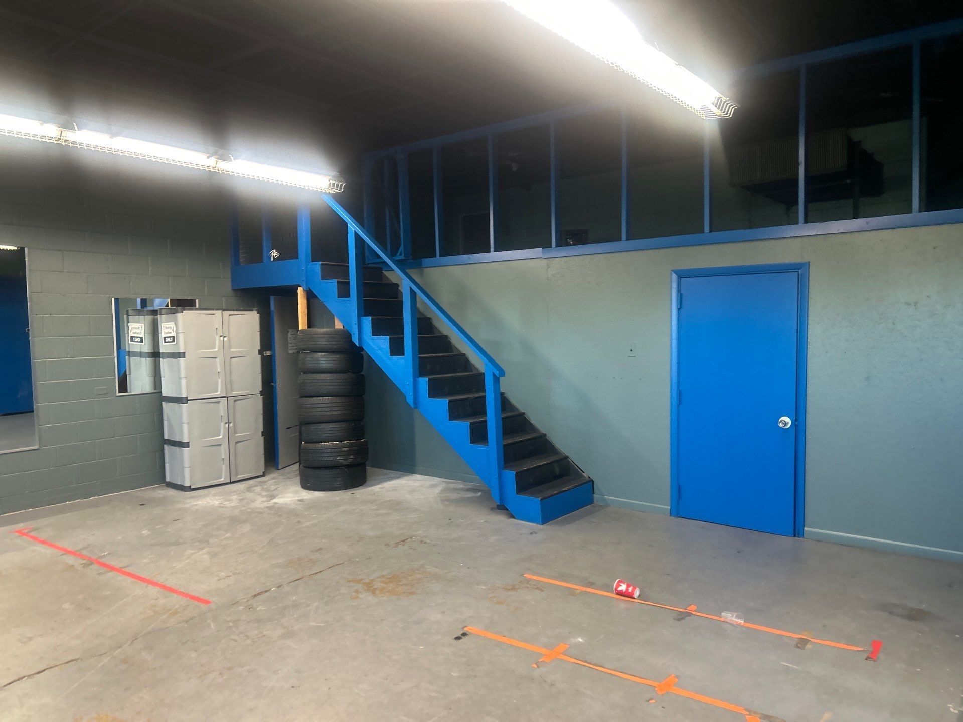 Empty room with blue staircase, blue door, stacked boxes, and fluorescent lights.