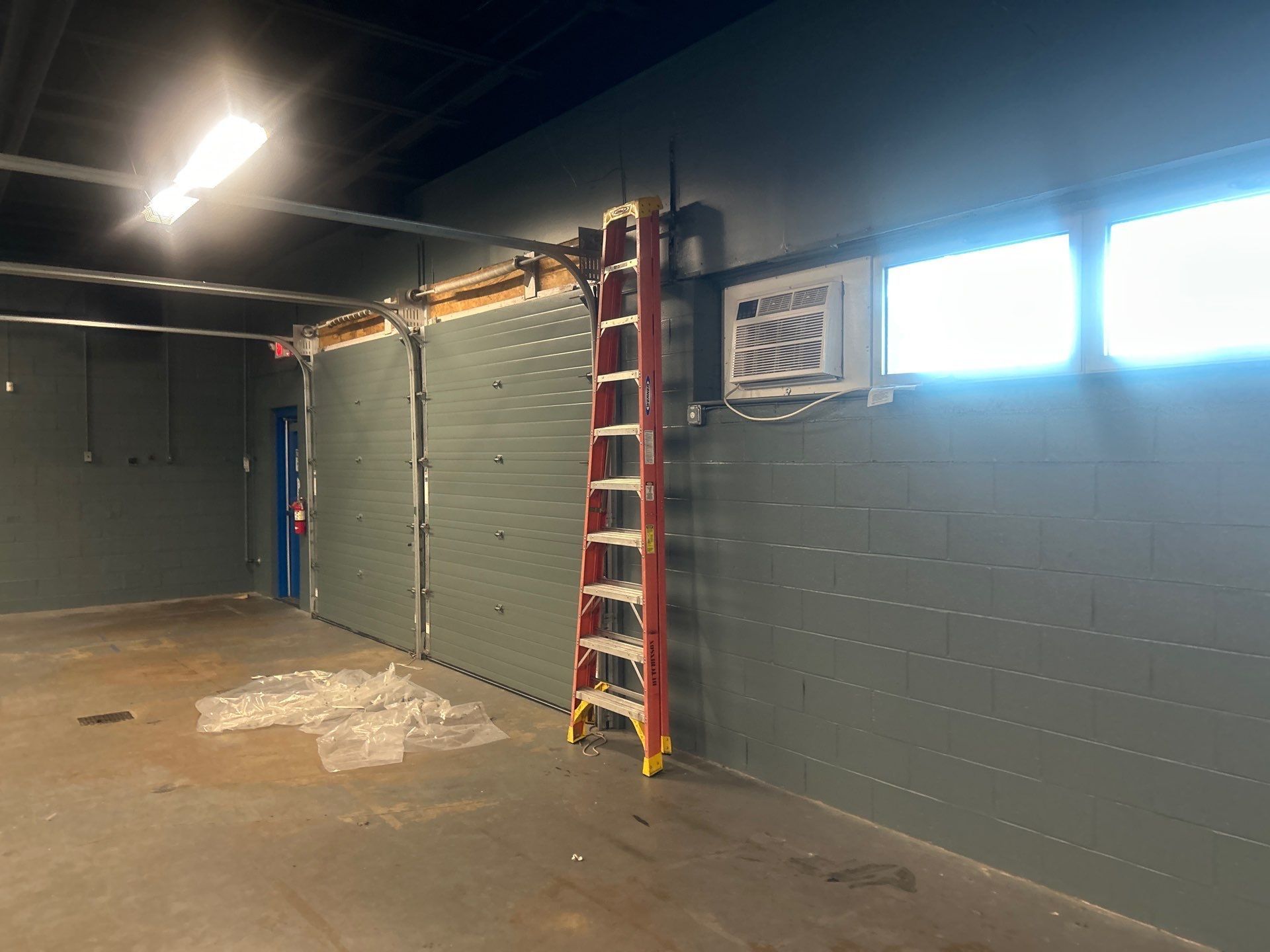 Dim wall with a red ladder, overhead lights, and a window AC unit on the right