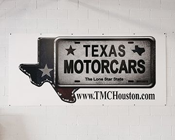 A sign for texas motorcars is hanging on a white brick wall.