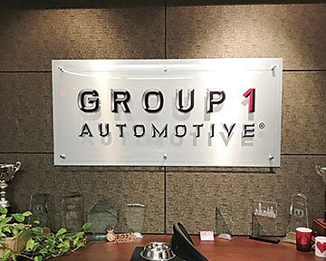 A group 1 automotive sign is hanging on a wall above a desk.