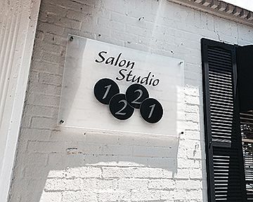 A salon studio sign is on a white brick wall.