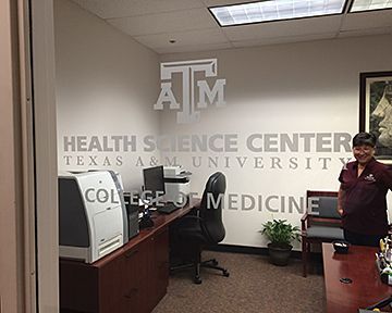 A woman is standing in a room with a sign that says health science center texas a & m university college of medicine