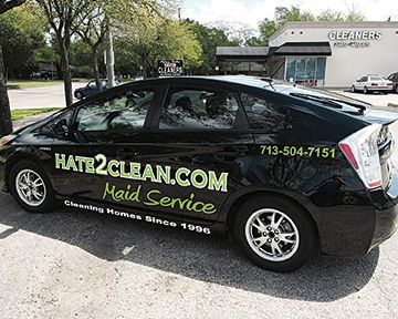 A black car with a maid service advertisement on the side is parked in a parking lot.