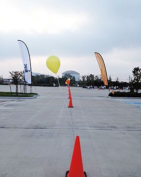 A yellow balloon is tied to a traffic cone in a parking lot