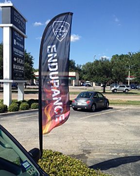 A car is parked in a parking lot next to a flag that says endurance.