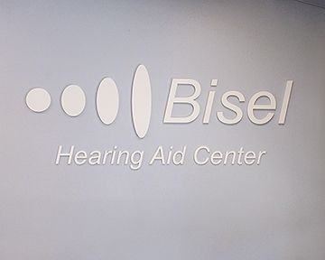 The logo for the bisel hearing aid center is on a white wall.