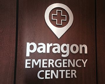 A sign for the paragon emergency center is on a wooden wall.