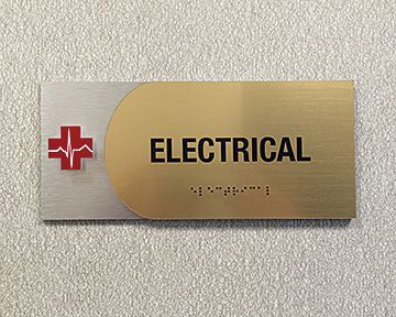 A gold and silver sign on a wall that says `` electrical ''.