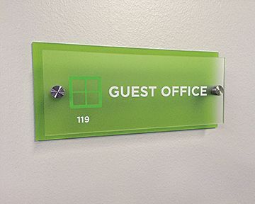 A green guest office sign is hanging on a white wall.