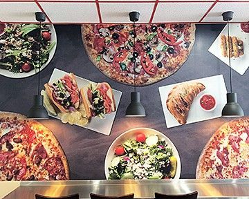 A restaurant with a lot of pizzas and sandwiches on the wall