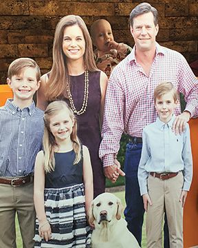 A family posing for a picture with a dog and a baby in the background.