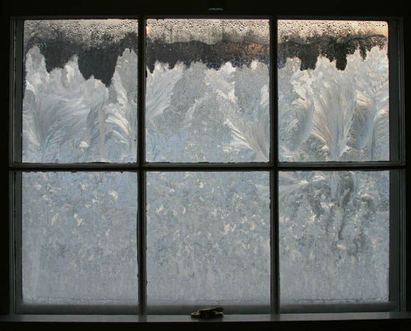 A window with frost on the glass and snow on the roof.