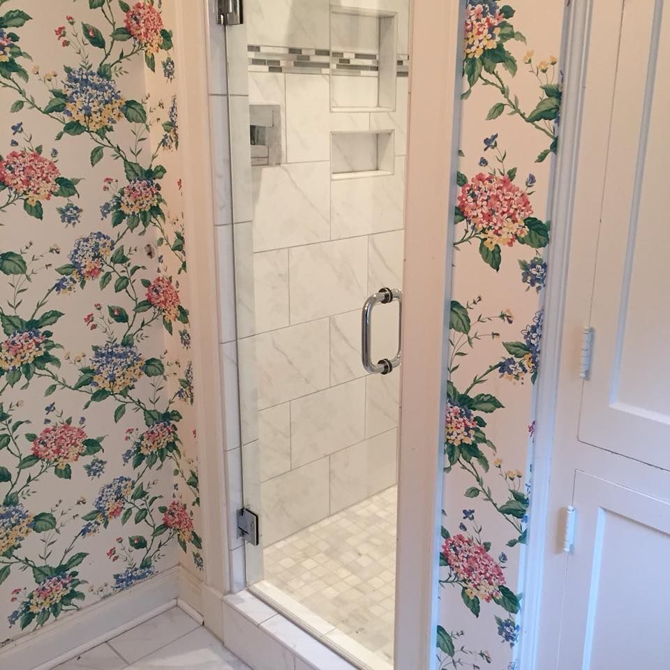 A bathroom with floral wallpaper and a glass shower door