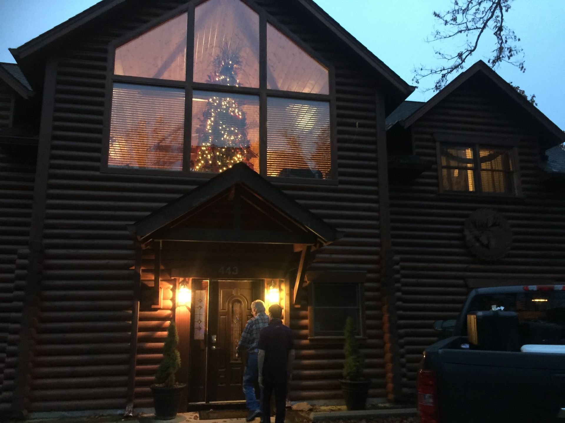 A large log cabin with a christmas tree in the window
