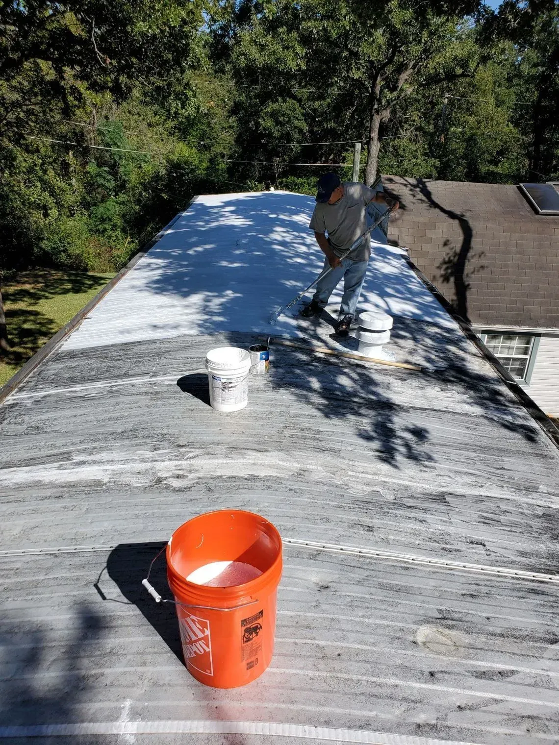 Person coating a flat roof with white sealant. Buckets of sealant on the roof.