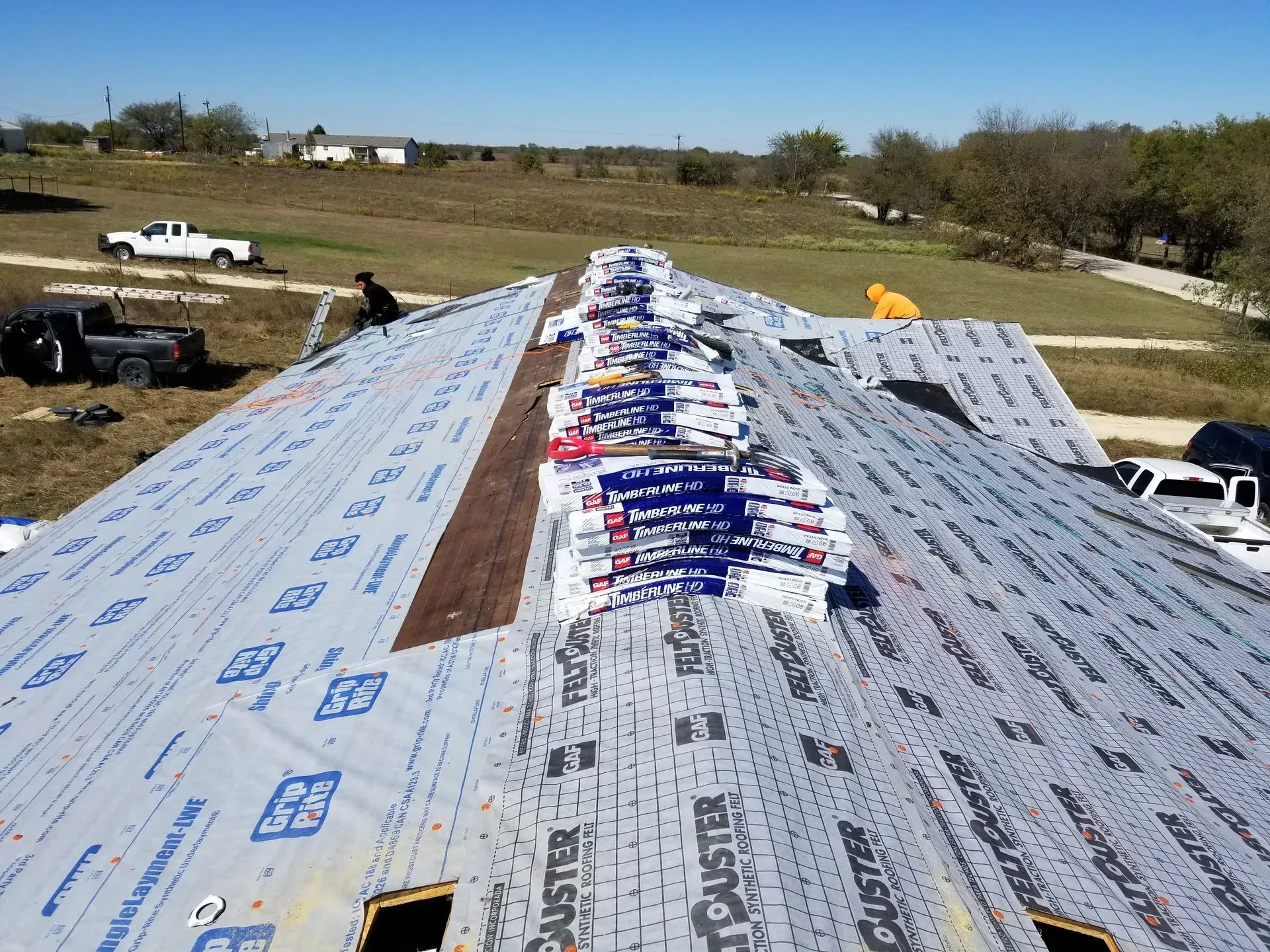 Workers installing roofing shingles on a house; bundles of shingles line the roof.