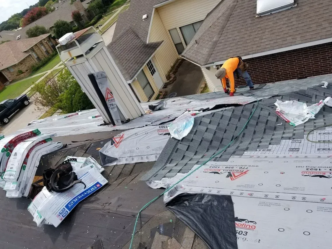 Roofer works on a roof, surrounded by shingles and materials.