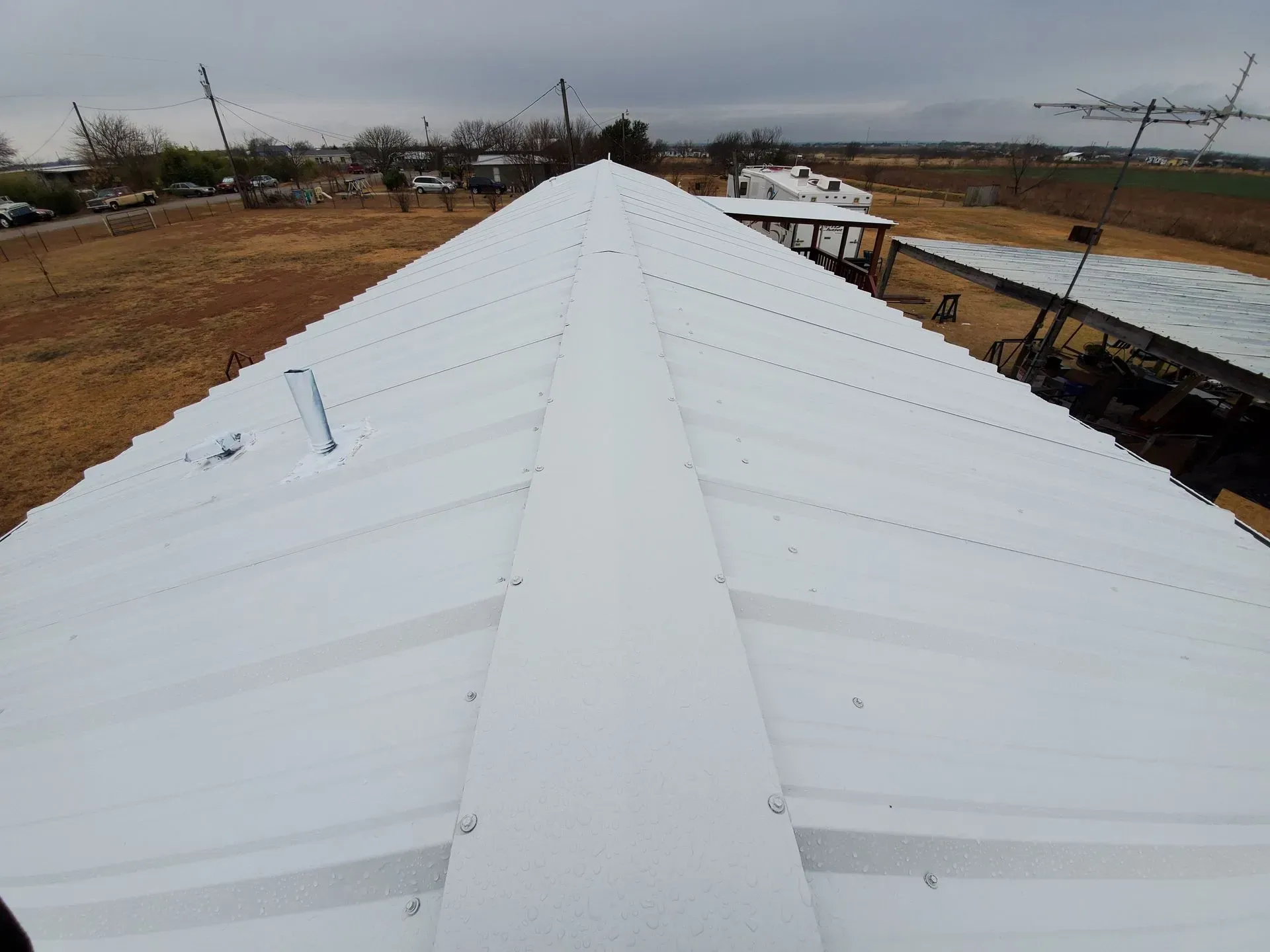View of a white metal roof with a central ridge, outdoors on a cloudy day.