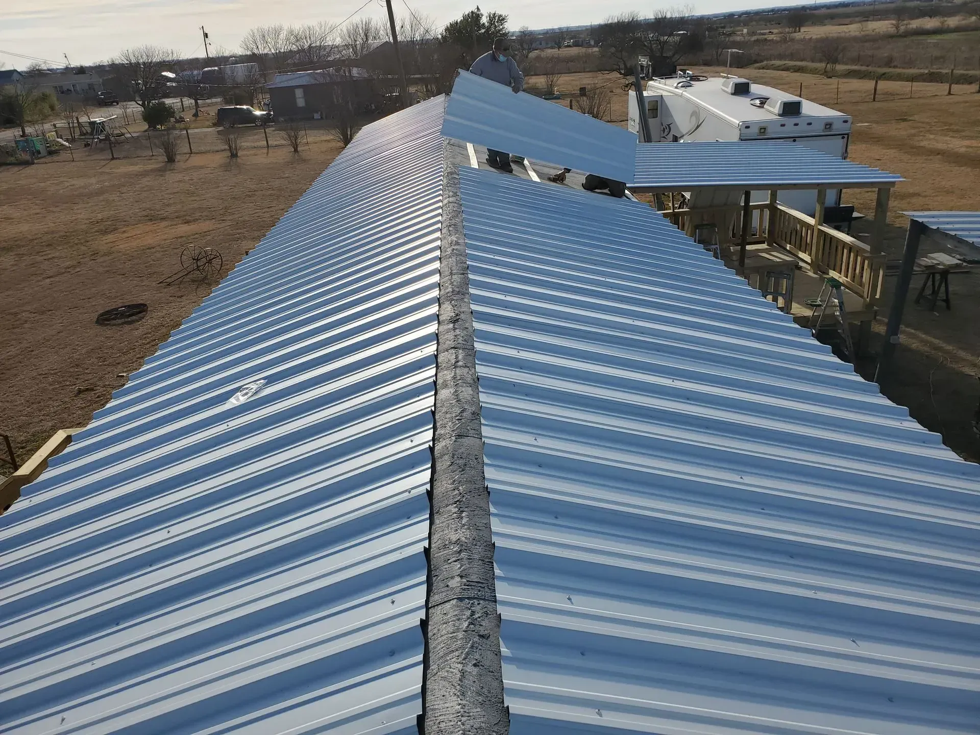 Metal corrugated roof, shiny and reflective, spanning a long structure outdoors.