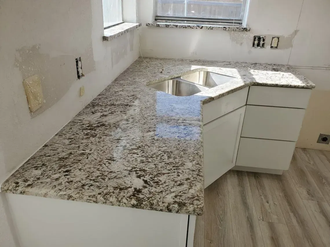 Kitchen counter with granite countertop, white cabinets, and stainless steel sink.