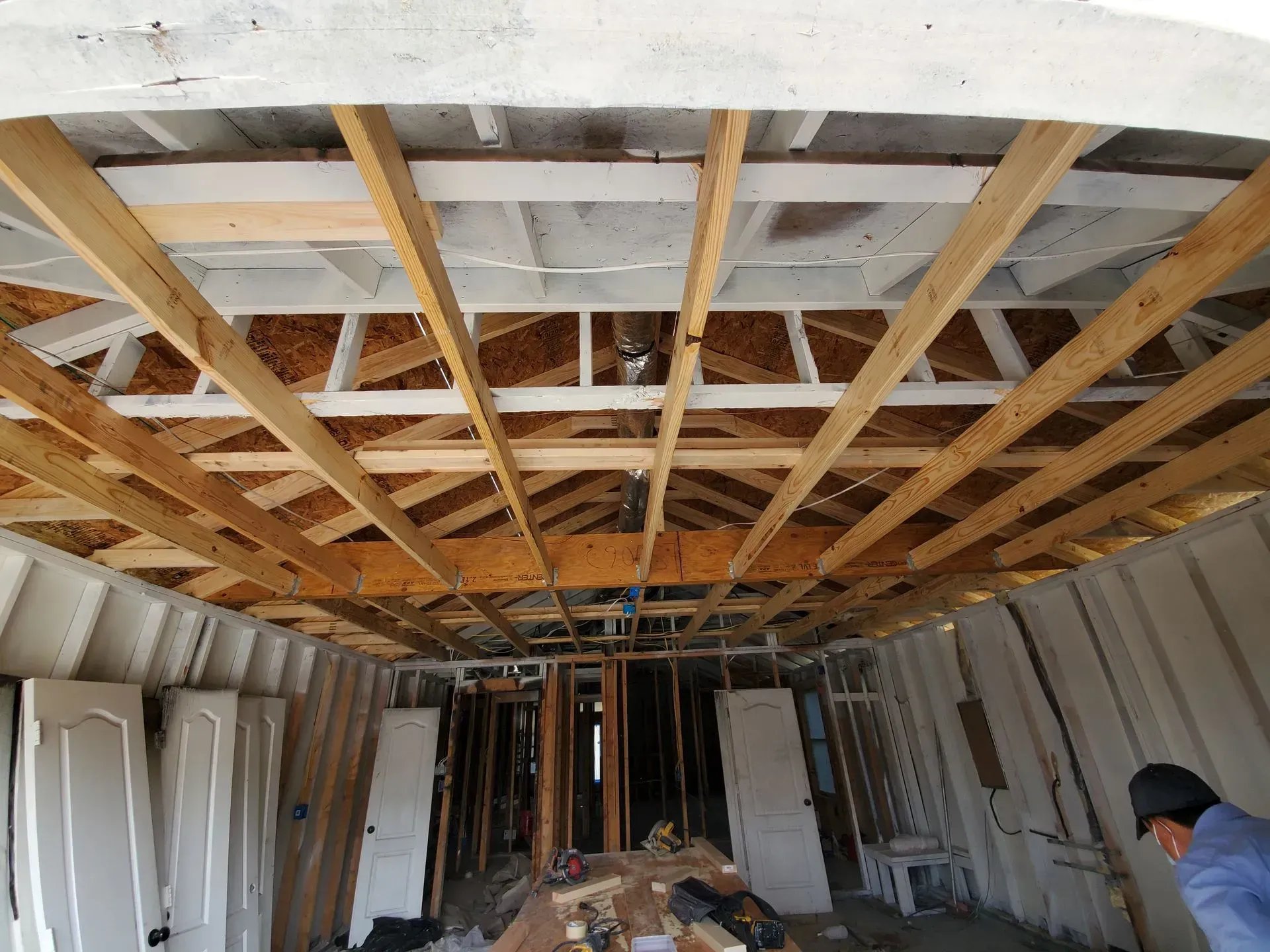 Interior view of a building under construction. Visible are exposed ceiling beams, doors, and a person.