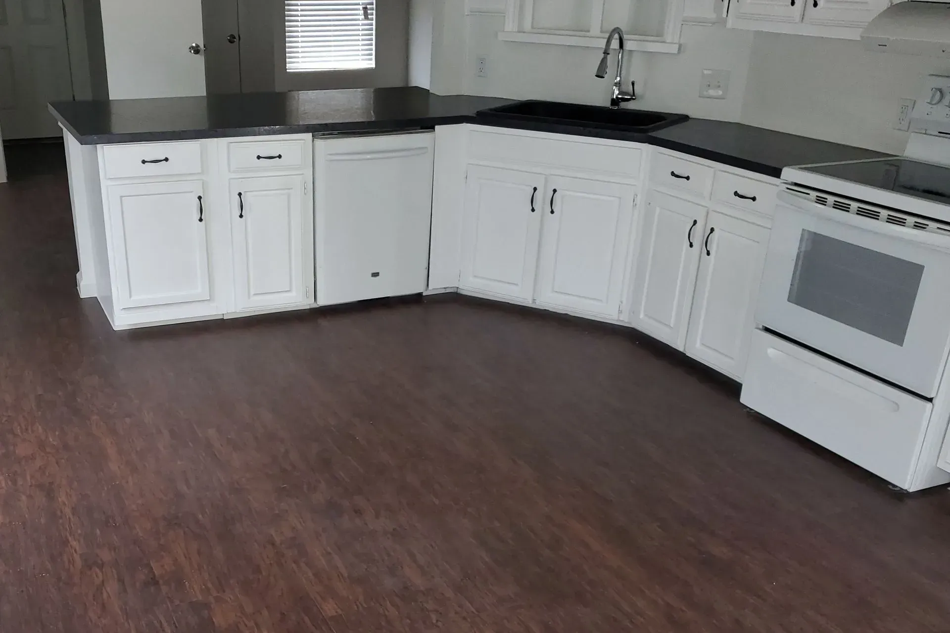White kitchen cabinets with black countertops and appliances, wooden floor.