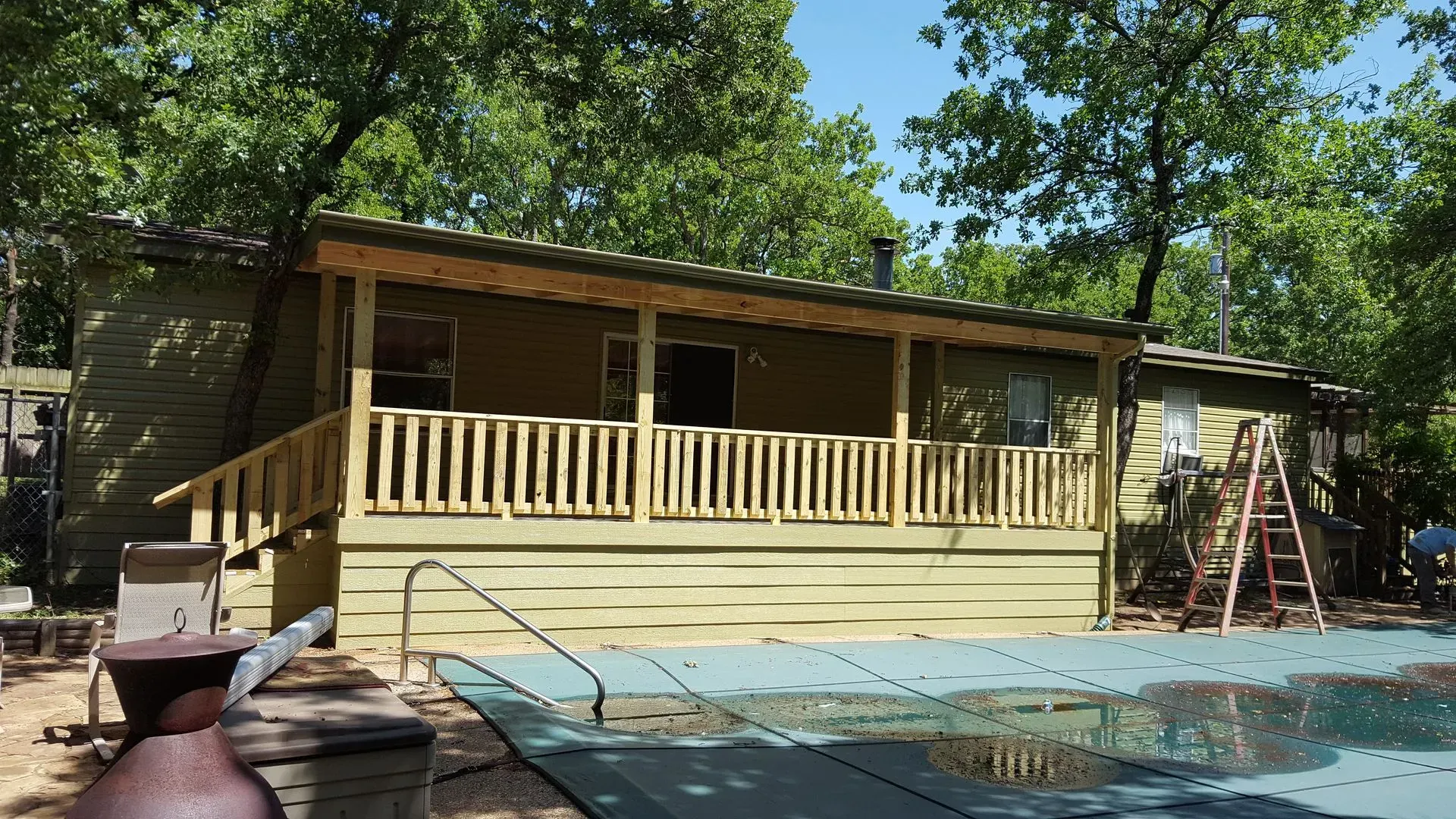 A cabin with a porch and pool in a wooded area, partially covered pool.