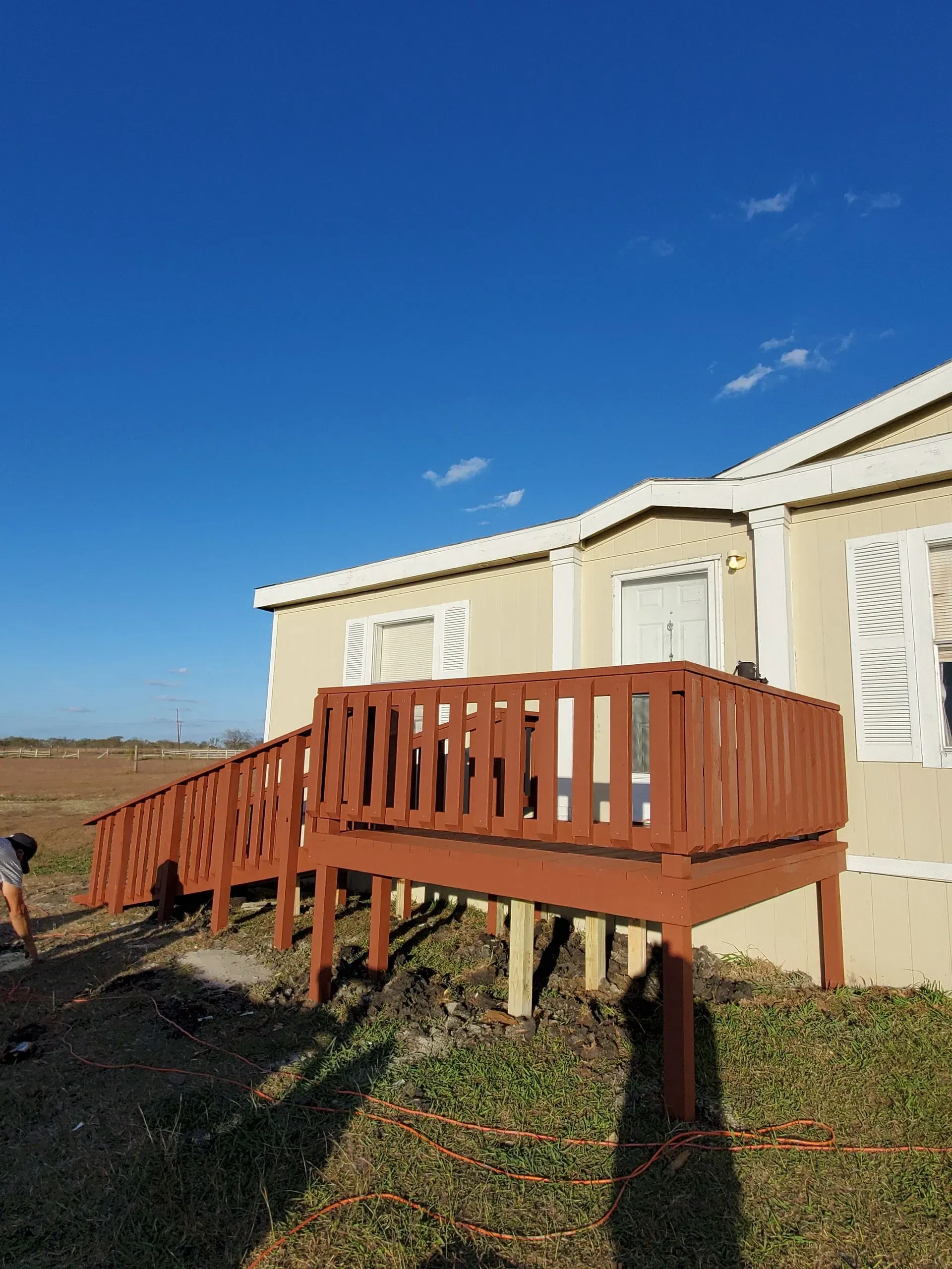 Brown wooden deck with railings, attached to a tan building against a blue sky.