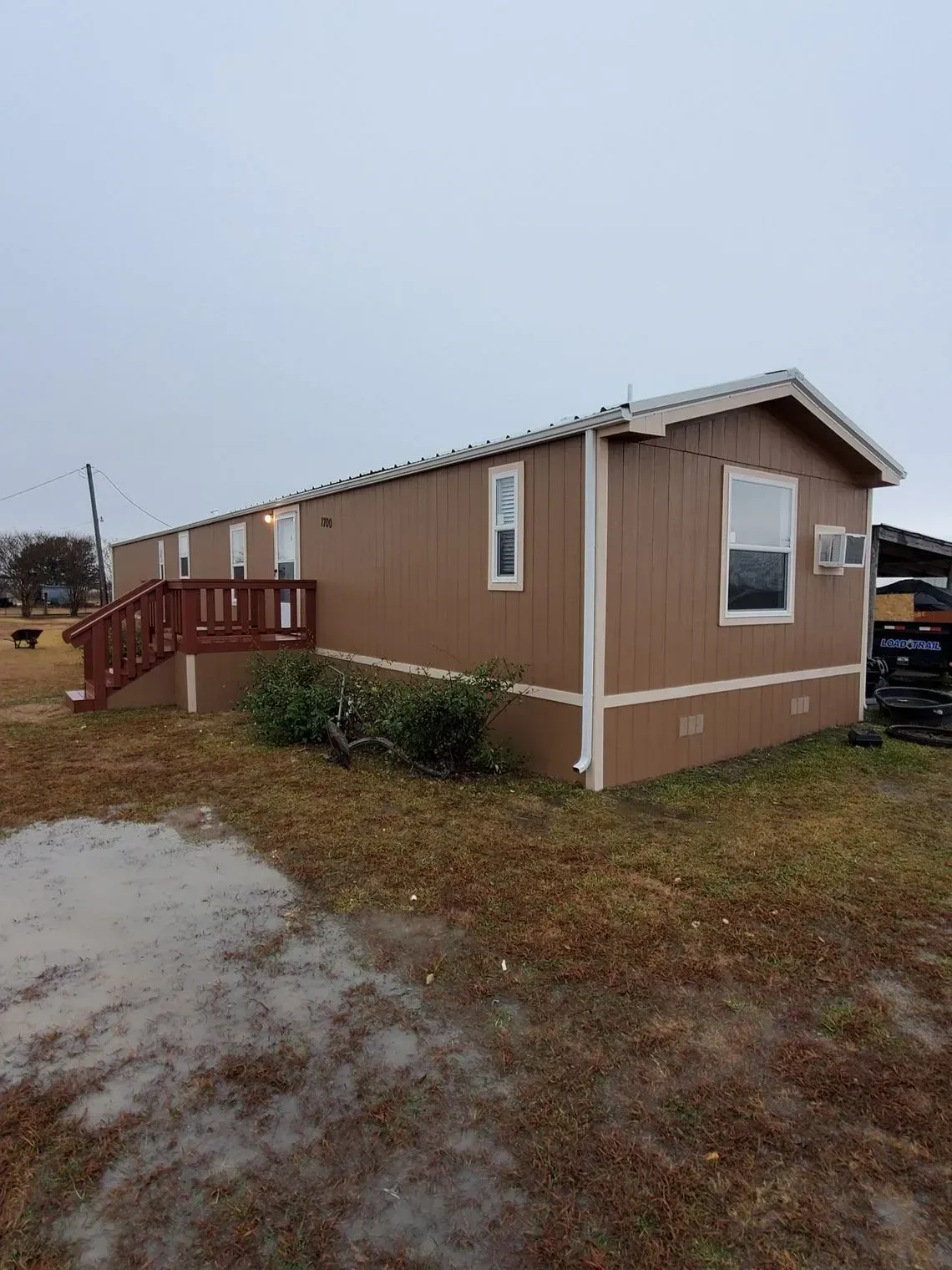 Brown mobile home with white trim and a small porch on a cloudy day.