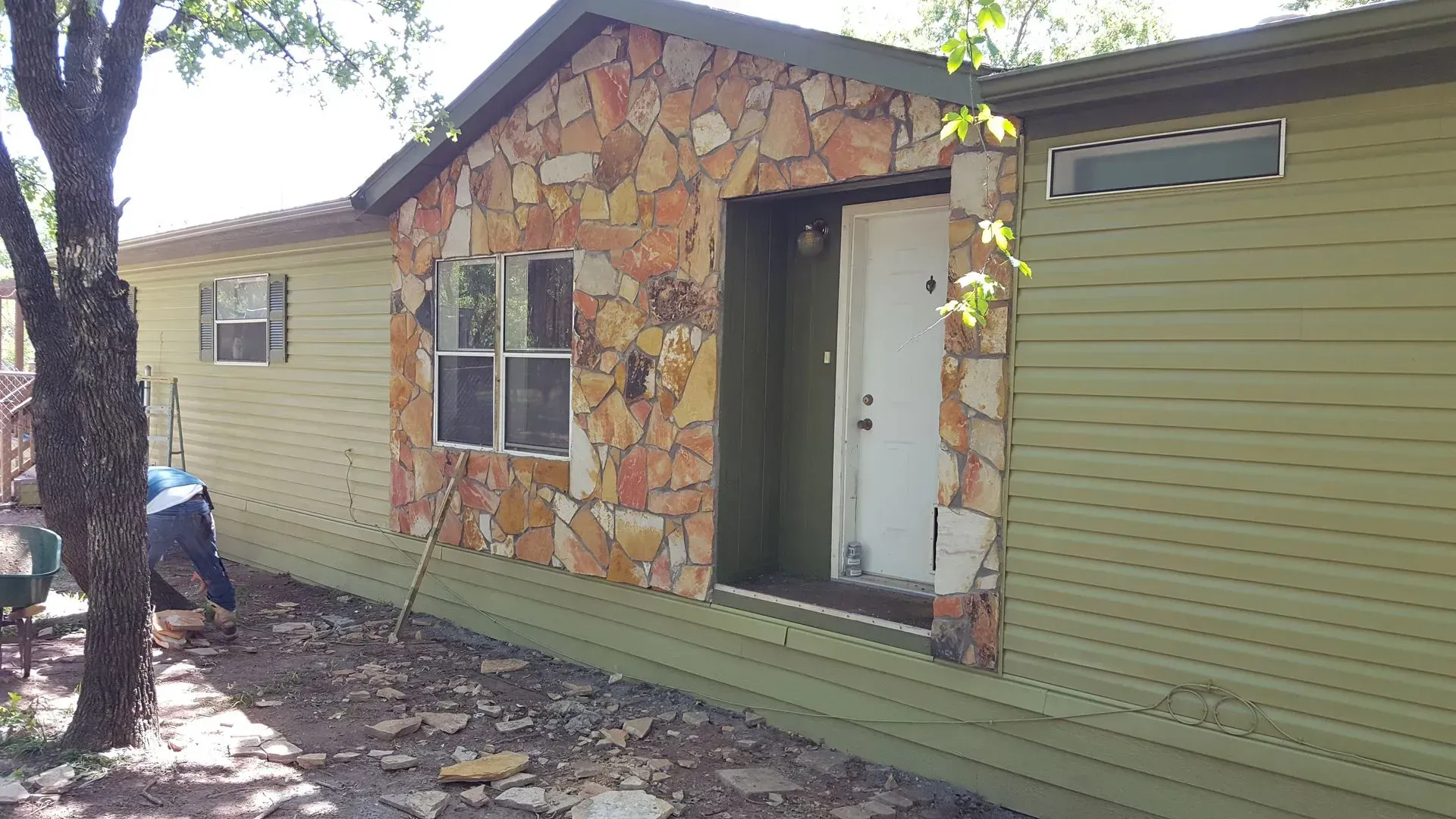 House exterior with stone facade around the entry and a person working in the yard.