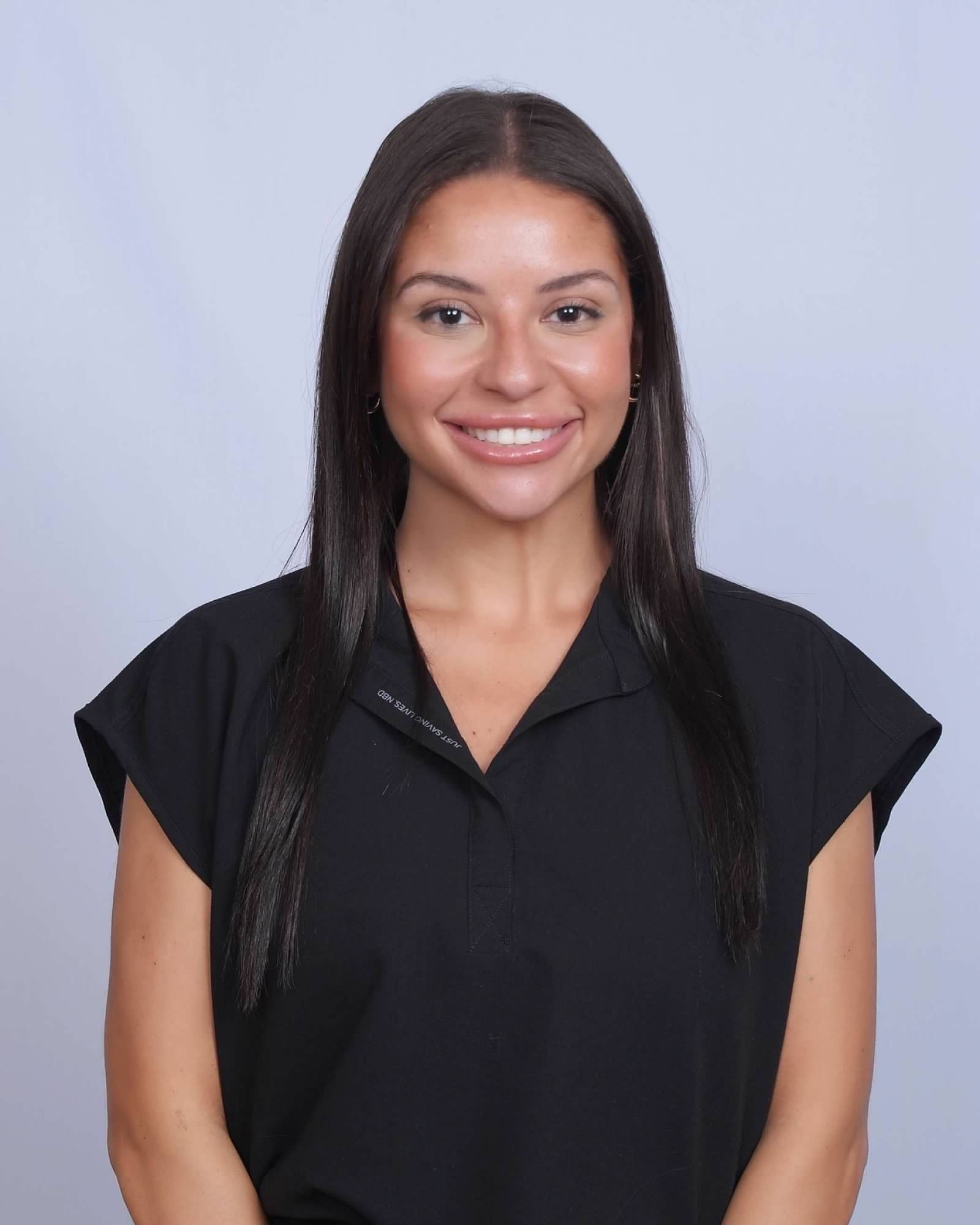 Woman with dark hair smiling, wearing a black shirt, against a light blue background.