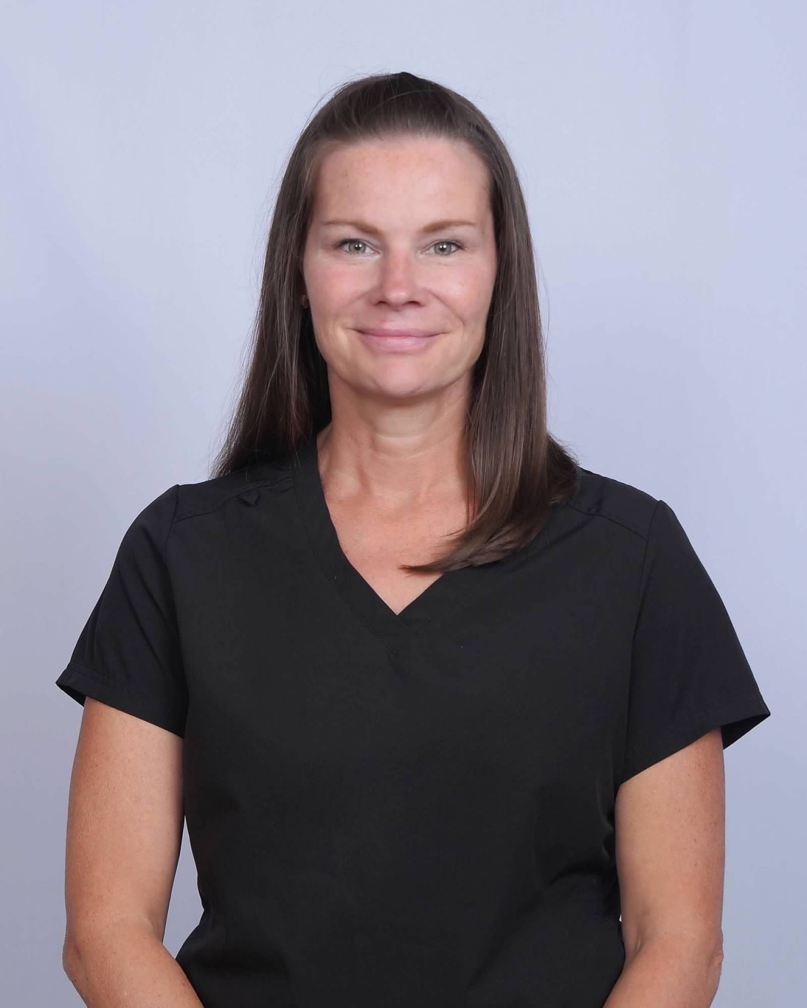 Woman with shoulder-length brown hair wearing a black V-neck shirt, smiling against a light blue background.