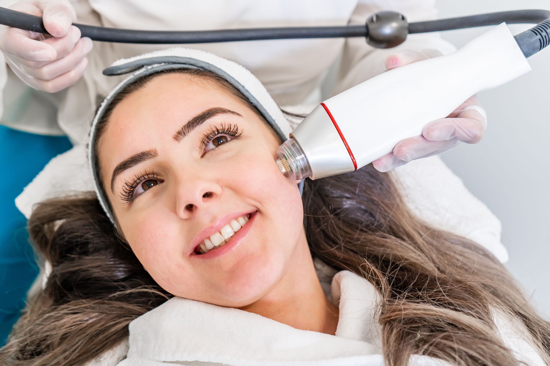 Woman receiving a facial laser treatment at a clinic, smiling.
