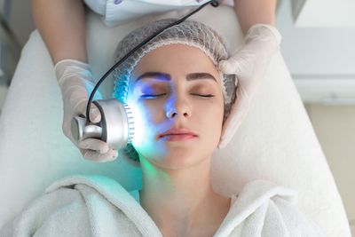 Woman receiving a facial treatment with glowing blue device in a spa bed