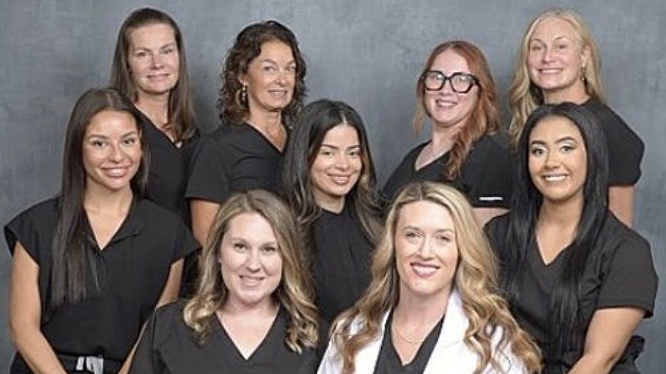 Group of women smiling, dressed in black, posing against a gray background.