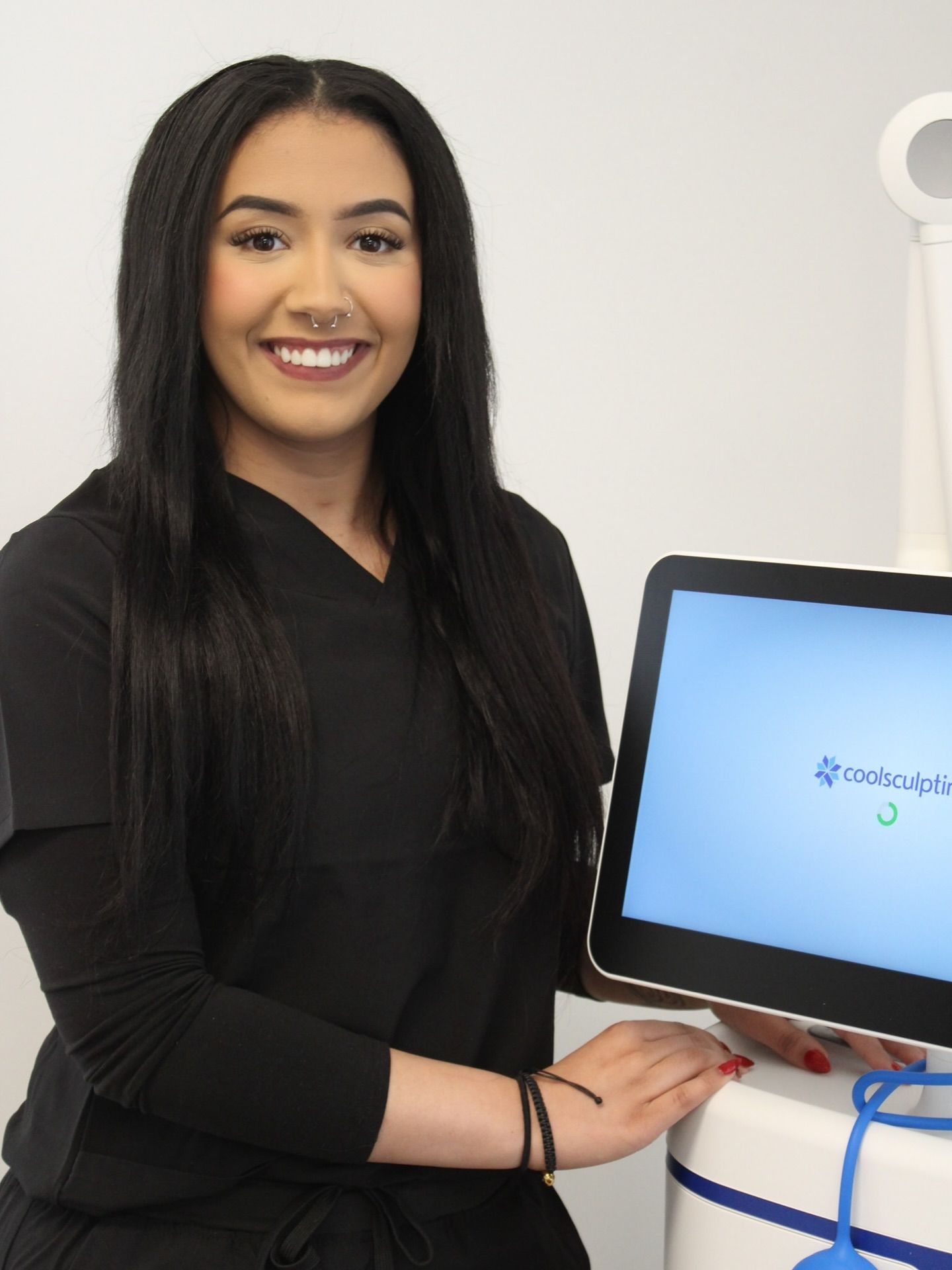 Woman in black scrubs smiling, holding a tablet displaying a medical logo.