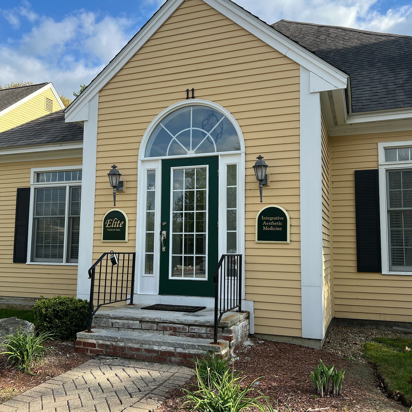 Yellow building with green door, black shutters, and brick walkway.