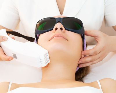 Facial treatment with a handheld device applied to a reclining person wearing dark protective goggles