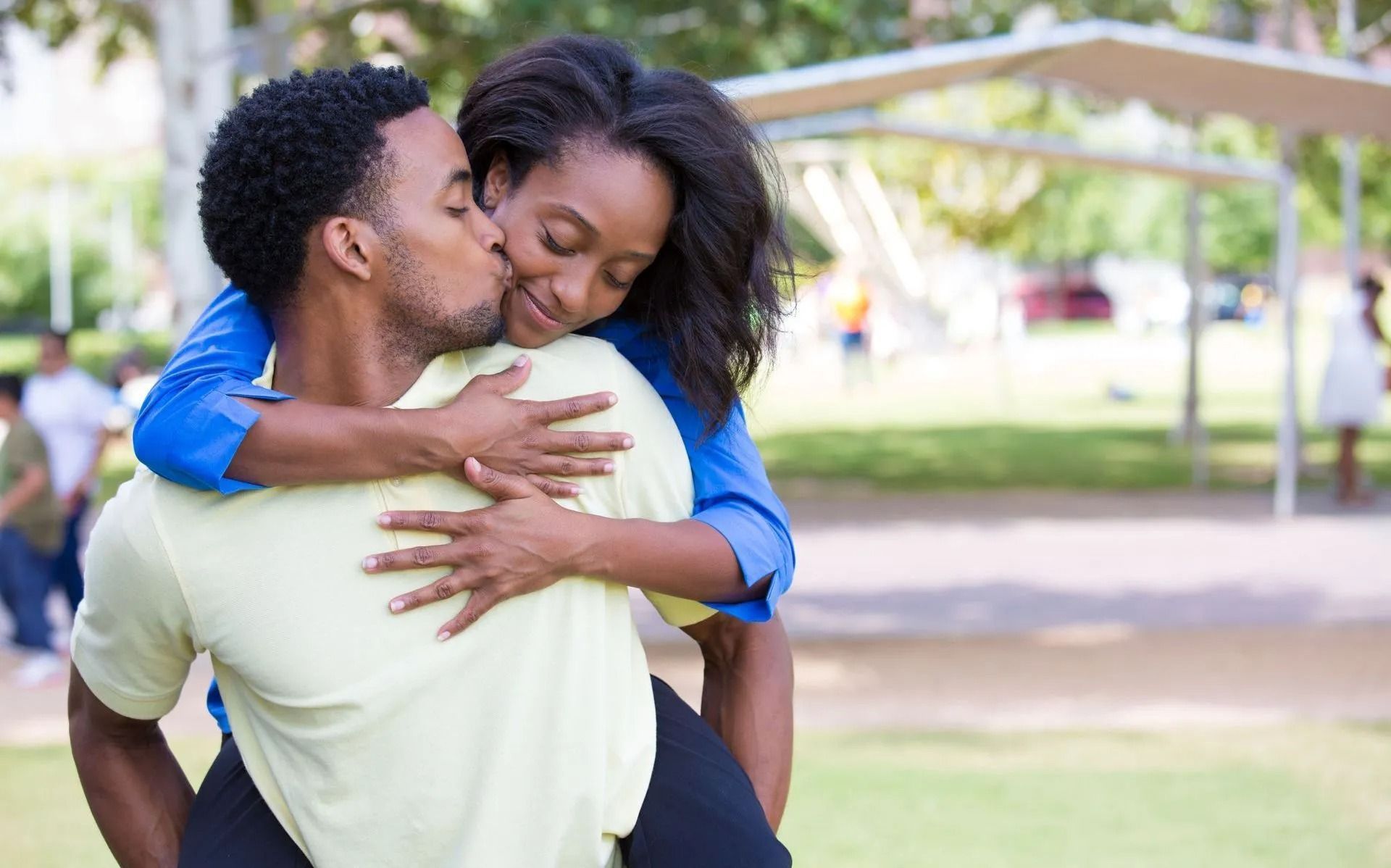 Couple embracing outdoors, smiling in a park with greenery in the background