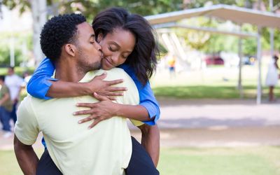 Couple embracing outdoors, smiling in a park with greenery in the background